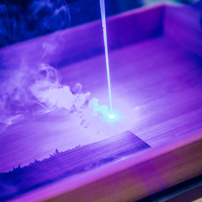 Small wooden box with a glowing stick inside, emitting smoke on a dark background